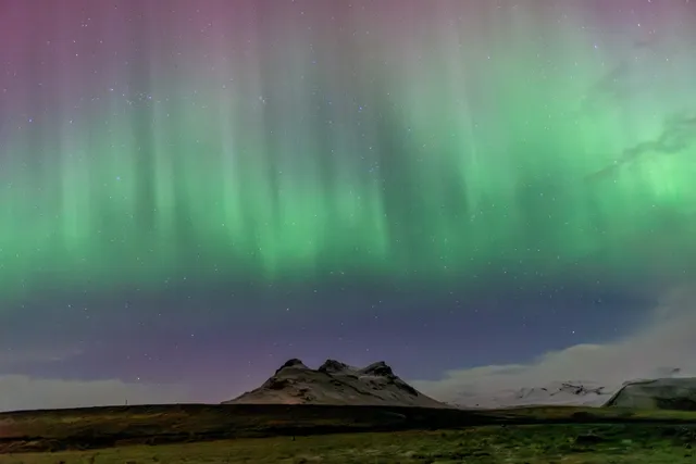 Intensa aurora boreal verde sobre una formación volcánica nevada y el paisaje glaciar de Mýrdalsjökull, cerca de Vík, en el sur de Islandia.